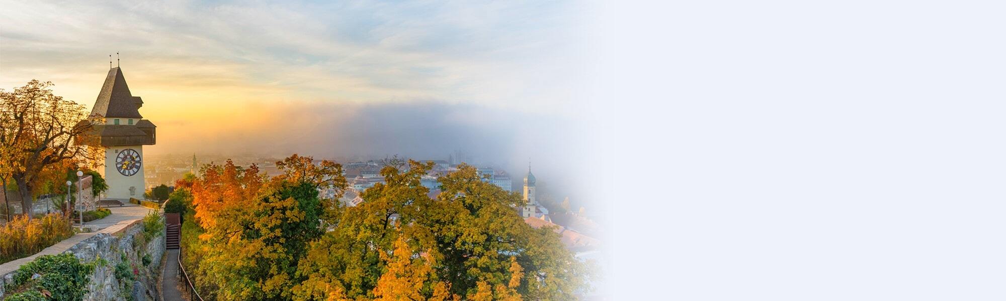 Der Uhrturm auf dem Grazer Schlossberg, umgeben von herbstlich gefärbten Bäumen